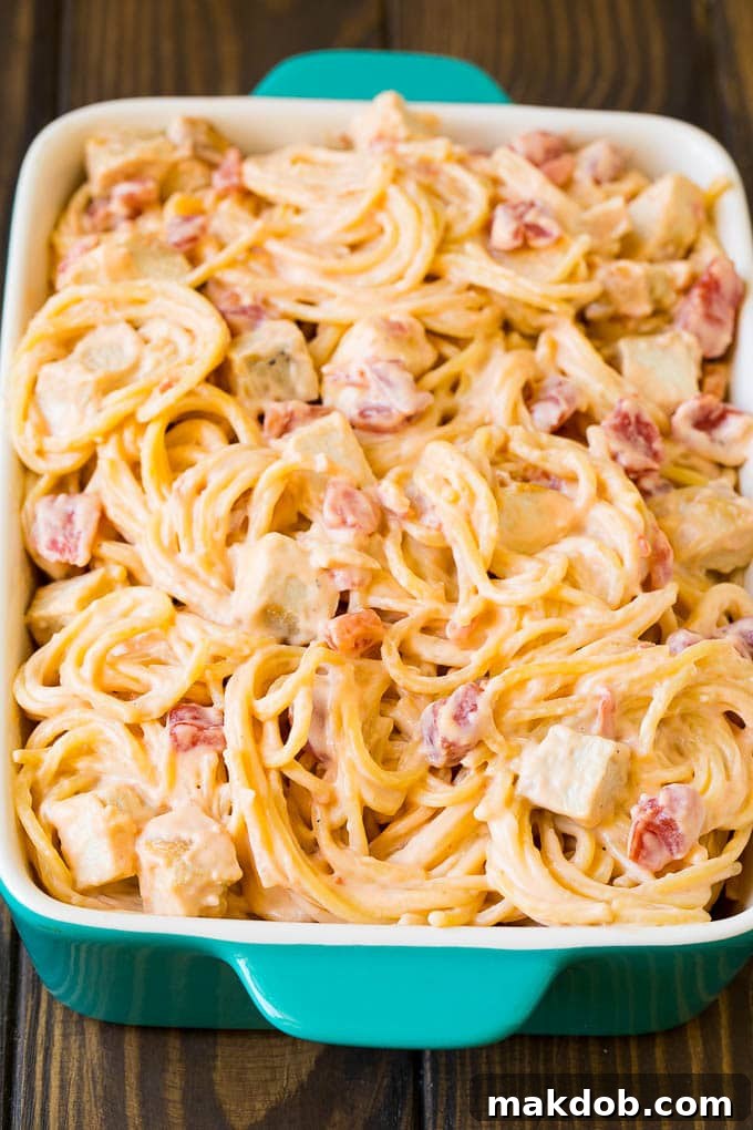 Cheesy spaghetti mixed with chicken and tomatoes in a baking dish, before being baked.