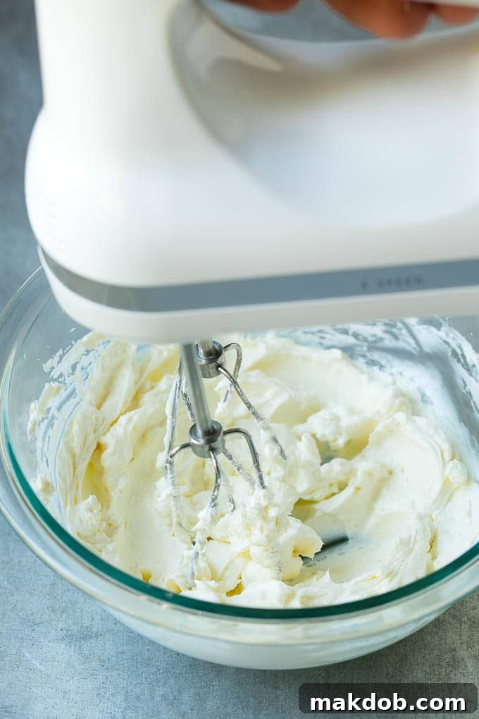 A mixer whipping up cream cheese in a bowl, showing the initial step of making the fruit dip smooth.
