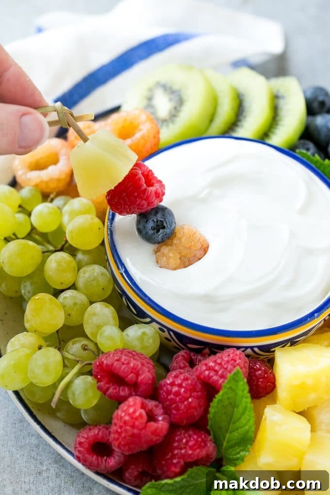 A skewer of berries being dipped into a bowl of creamy fruit dip, illustrating serving suggestion.
