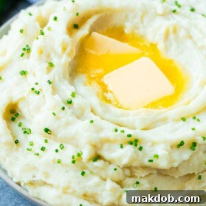 A generous bowl of fluffy Instant Pot mashed potatoes, elegantly topped with melting pats of butter and finely sliced chives.