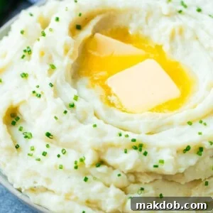 A fluffy bowl of Instant Pot mashed potatoes, beautifully topped with melting pats of butter and freshly sliced chives.