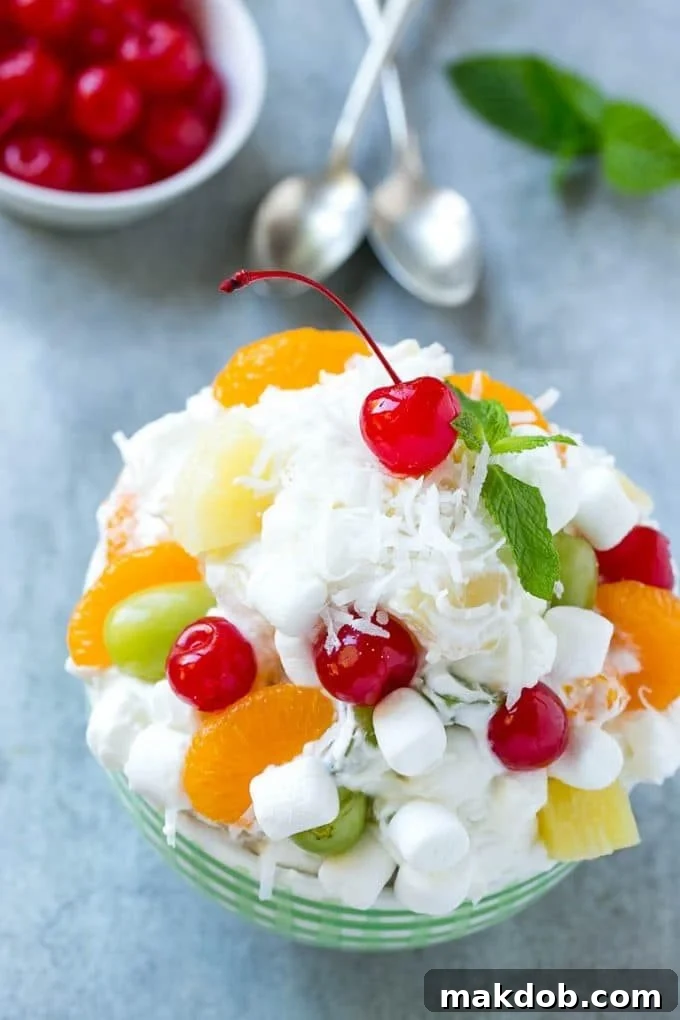 Ambrosia Salad Recipe | Fruit Salad | Potluck Dish #fruit #fruitsalad #coconut #marshmallows #dessert #dinneratthezoo A bowl of ambrosia salad topped with coconut and a cherry.