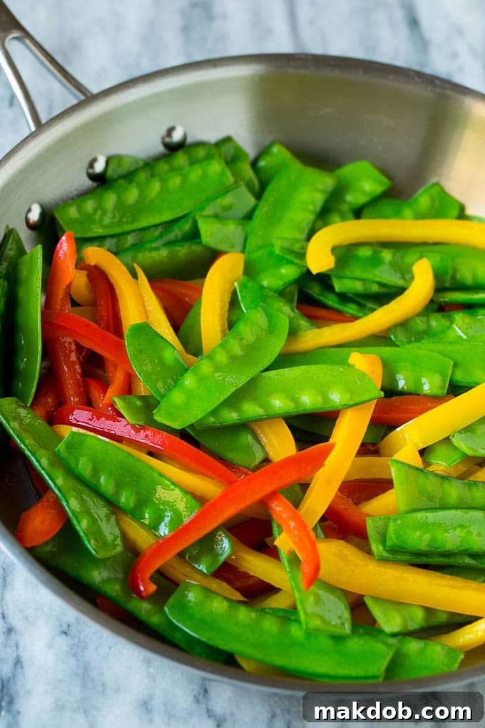 Cooked snow peas and bell peppers in a skillet.