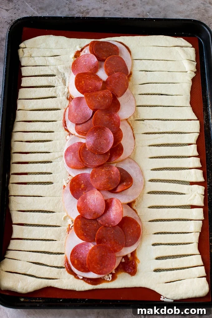 A sheet of pizza dough topped with tomato sauce, mozzarella cheese, pepperoni and Canadian bacon.