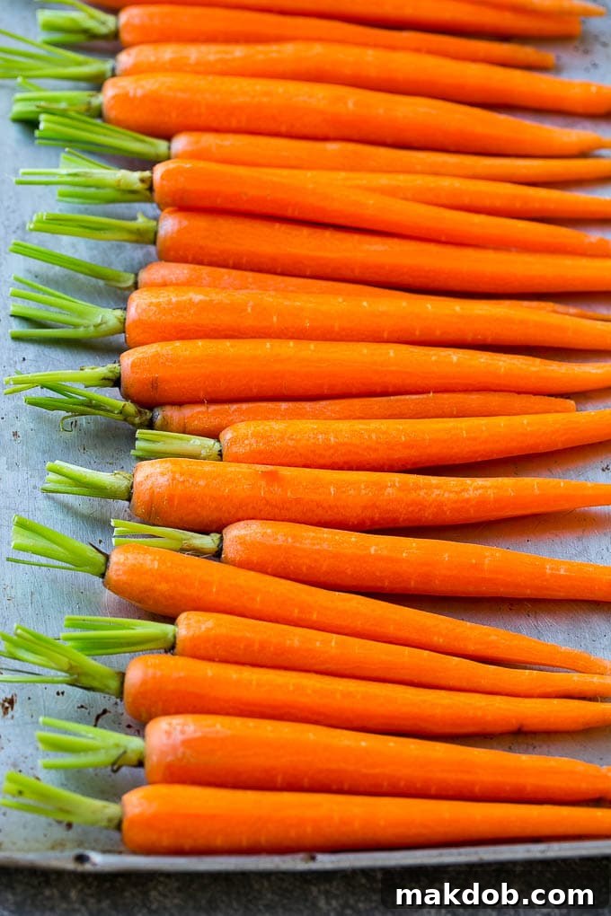 A row of peeled baby carrots on a baking pan.