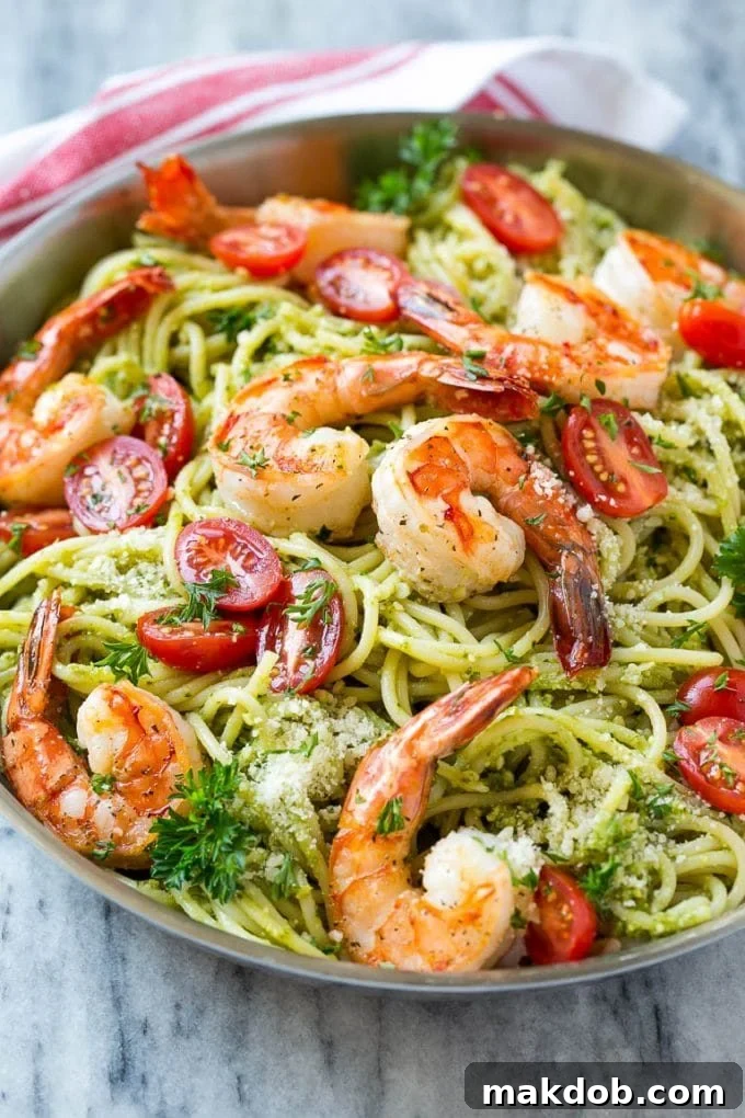 A pan of shrimp pesto pasta topped with tomatoes, parmesan cheese and parsley.