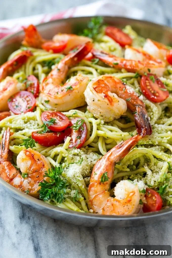 A delightful dish of pesto pasta with expertly seared shrimp, halved cherry tomatoes, and a dusting of Parmesan cheese, ready to be enjoyed.