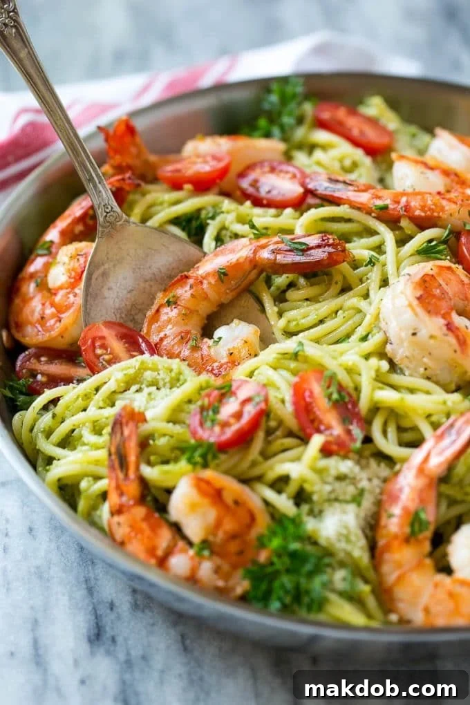 A serving spoon filled with a luscious portion of pesto pasta and a perfectly cooked shrimp, inviting you to savor every bite.