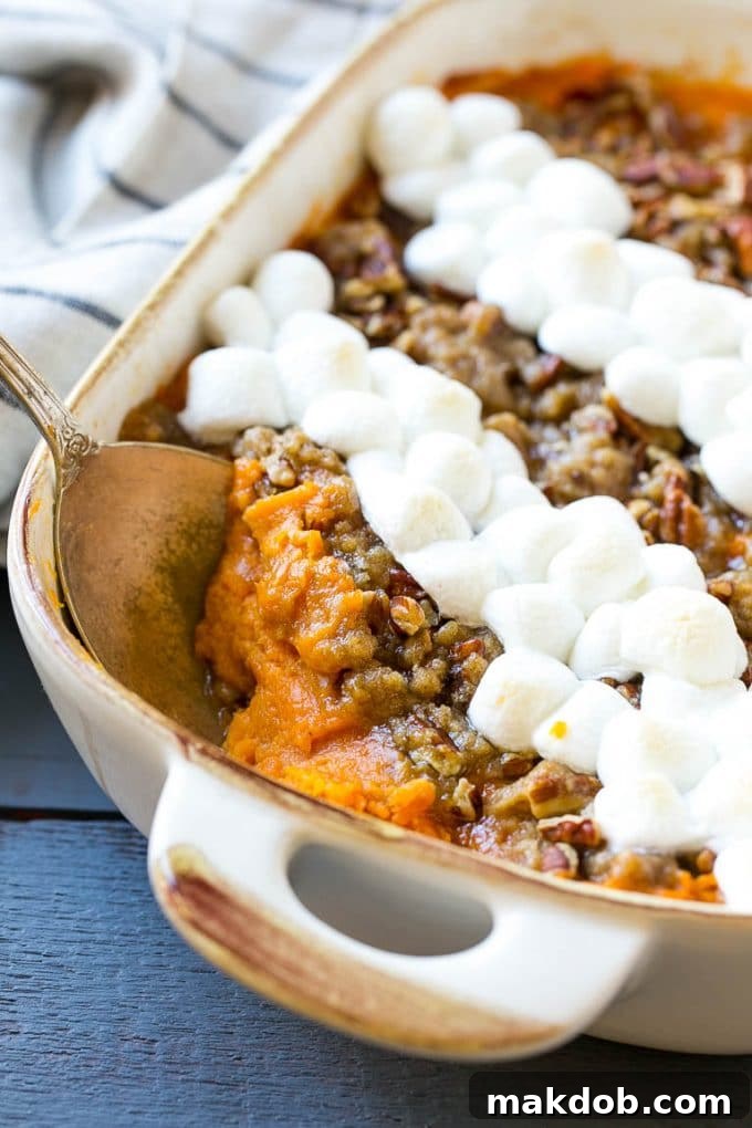 Sweet Potato Casserole with Marshmallows in a white baking dish with a serving spoon in it.