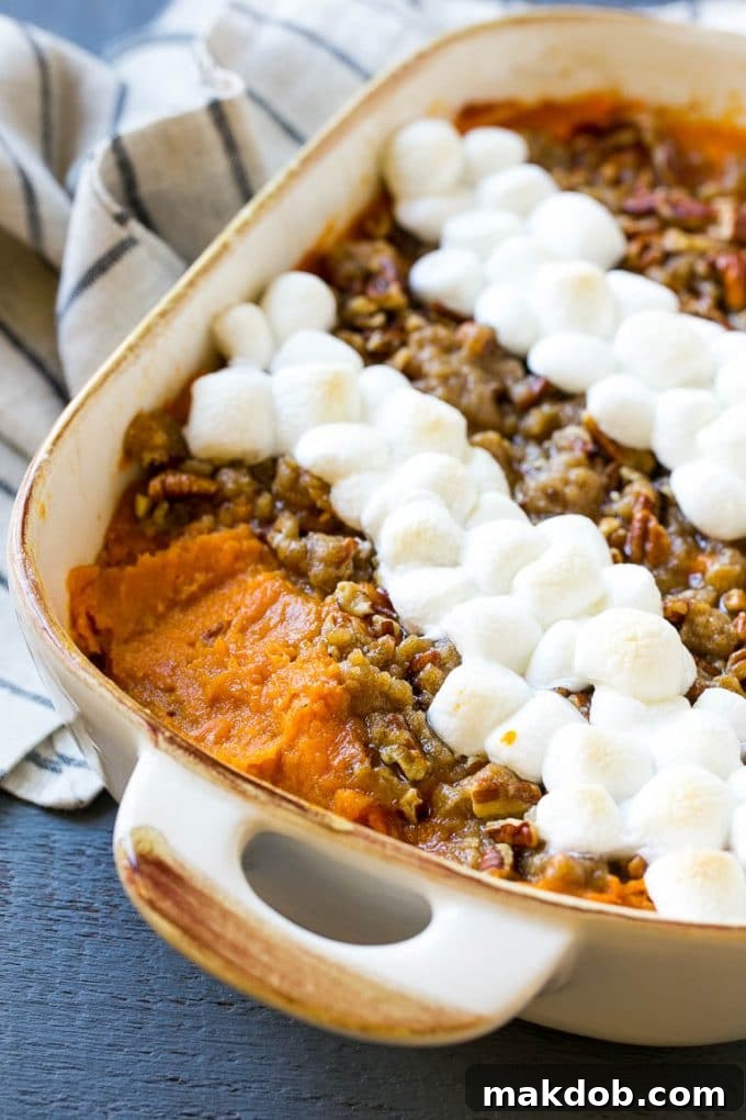 This recipe for sweet potato casserole with marshmallows is mashed spiced sweet potatoes, topped with both a pecan streusel topping and plenty of mini marshmallows. A holiday classic that's a family favorite! A sweet potato casserole with a generous scoop removed, revealing the creamy interior beneath the pecan streusel and toasted marshmallows.