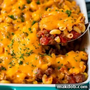 A spoon serving a hearty portion of hamburger casserole, rich with pasta and melted cheese.