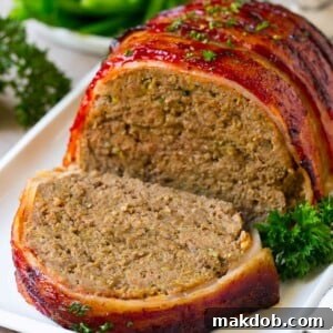 A bacon wrapped meatloaf with a slice out of it, on a serving platter, showcasing its savory layers.
