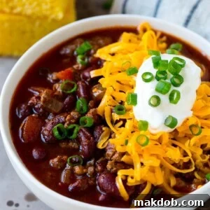 A hearty bowl of slow cooker chili, generously topped with shredded cheese, creamy sour cream, and vibrant green onions.