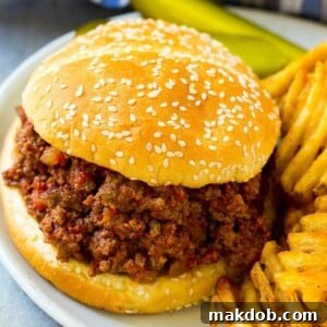 A classic slow cooker sloppy joe served on a soft bun, accompanied by crispy fries and tangy pickles.