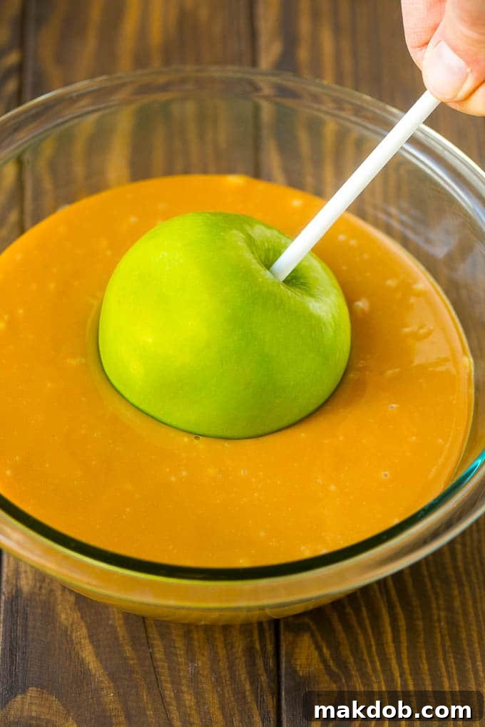 A green apple being dipped into a bowl of melted caramel.