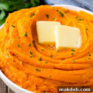 A rich bowl of creamy mashed sweet potatoes, elegantly topped with a melting pat of butter and a sprinkle of fresh parsley for a touch of color.