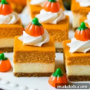 A stunning platter of pumpkin cheesecake bars, elegantly topped with swirls of whipped cream and adorable candy pumpkins, perfect for a festive fall treat.