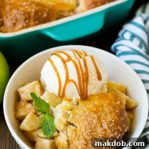 A warm, inviting apple cobbler, generously served with a scoop of melting vanilla ice cream and a luscious drizzle of caramel sauce, perfect for dessert.