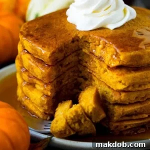 A tall stack of fluffy pumpkin pancakes, with a fork holding perfectly cut pieces, inviting you to enjoy a warm, comforting breakfast.