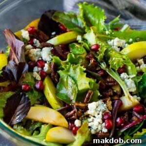 A bowl of vibrant pear salad featuring fresh sliced pears, crimson pomegranate seeds, creamy blue cheese, and crunchy candied pecans, all beautifully arranged.