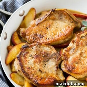A pan of tender apple pork chops, beautifully browned and nestled in a savory cider sauce with fresh apple slices and aromatic sage leaves.