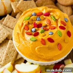 A vibrant pumpkin dip, beautifully presented with a variety of dippers including crisp apple slices, spicy gingersnap cookies, and wholesome graham crackers.