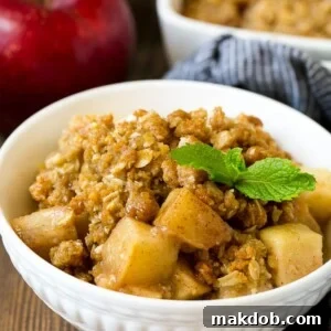A delightful bowl of apple crisp, beautifully garnished with a sprig of fresh mint, showcasing its golden, buttery oatmeal and walnut topping.