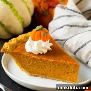A perfectly baked slice of homemade pumpkin pie, elegantly topped with a generous swirl of whipped cream and a charming candy pumpkin decoration.