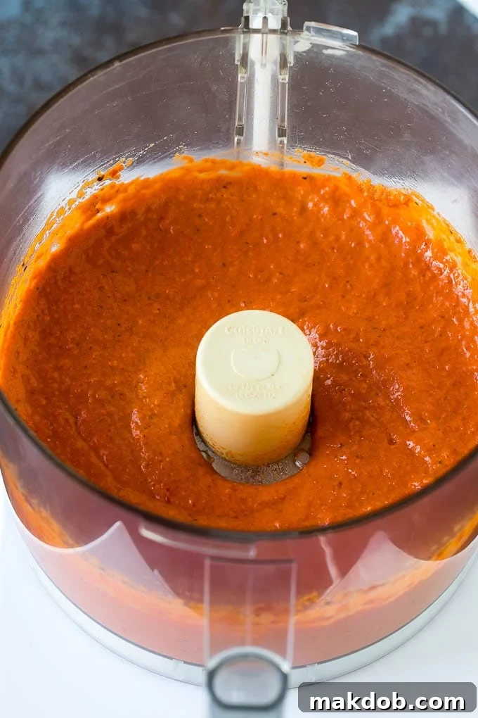 Vibrantly red muhammara dip being pureed to a smooth consistency in a food processor, highlighting the effortless and quick preparation of this delicious Middle Eastern delicacy.