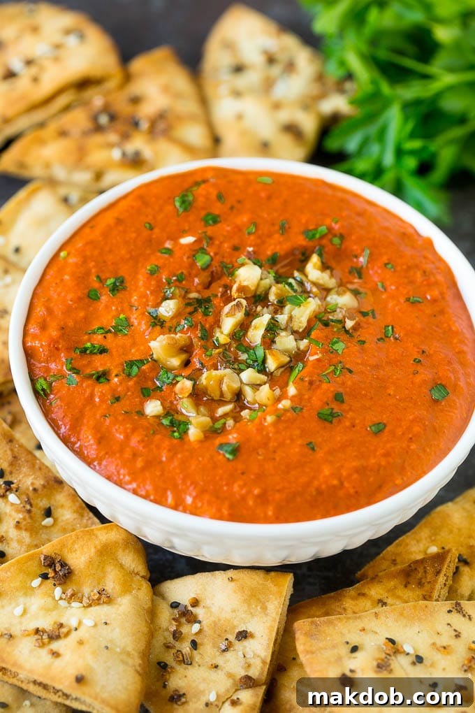 A close-up of a serving bowl filled with rich, creamy Muhammara dip, elegantly garnished with a generous sprinkle of chopped walnuts and vibrant fresh parsley.