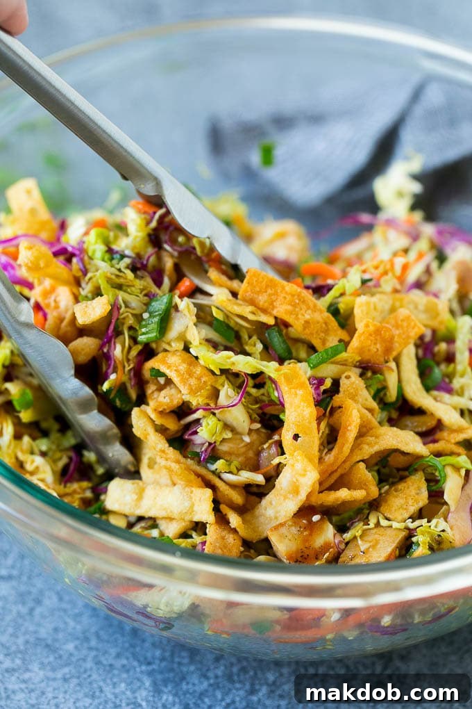 Tongs gracefully serving up a generous portion of freshly tossed Asian chicken salad from a large bowl, highlighting its abundant ingredients.