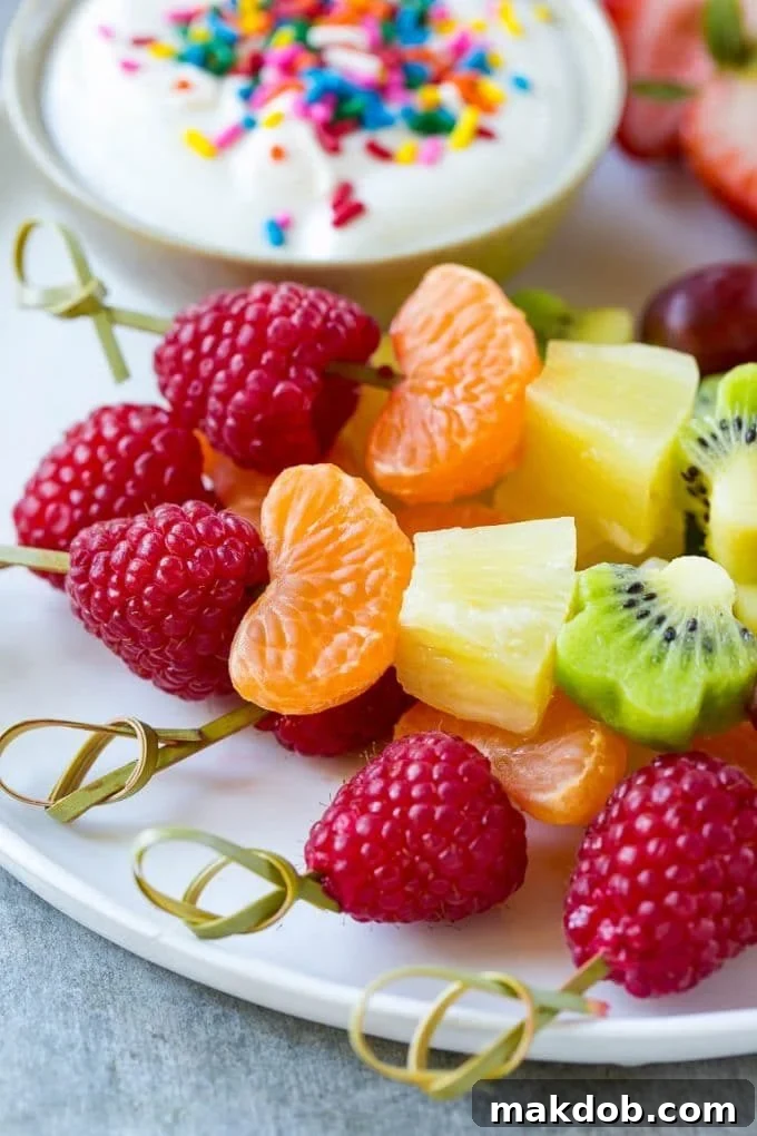 Close-up of freshly prepared fruit kabobs featuring kiwi, raspberries, grapes, and oranges, served alongside a sweet yogurt dipping sauce.