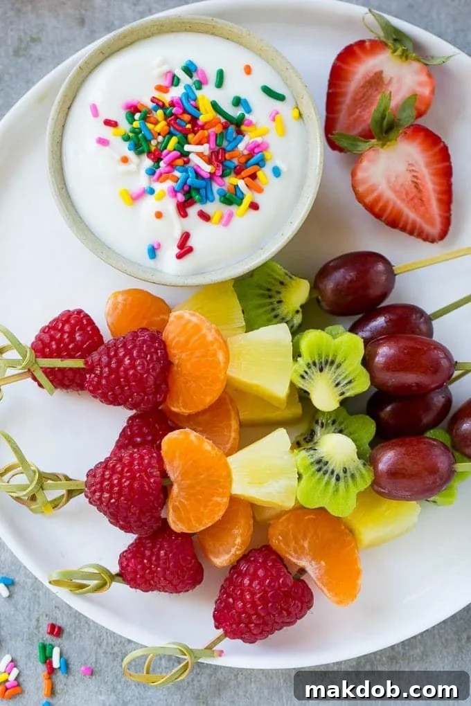 A vibrant platter showcasing an assortment of rainbow fruit skewers, accompanied by a small bowl of creamy yogurt sauce, ideal for sharing.
