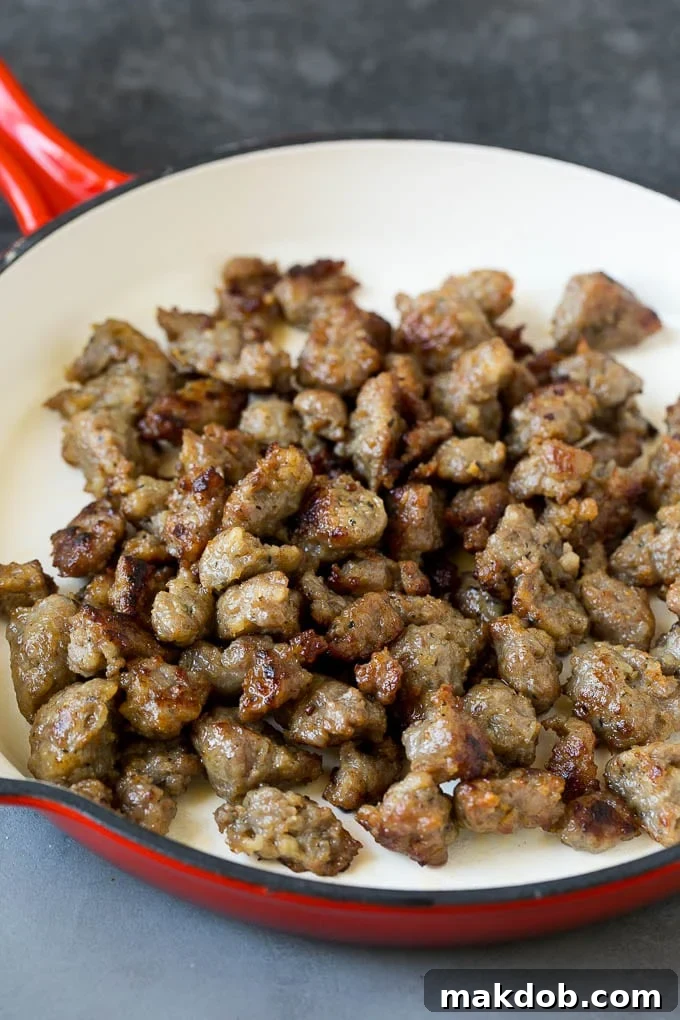Cooked sausage in a pan, browned and crumbled, ready for other ingredients.