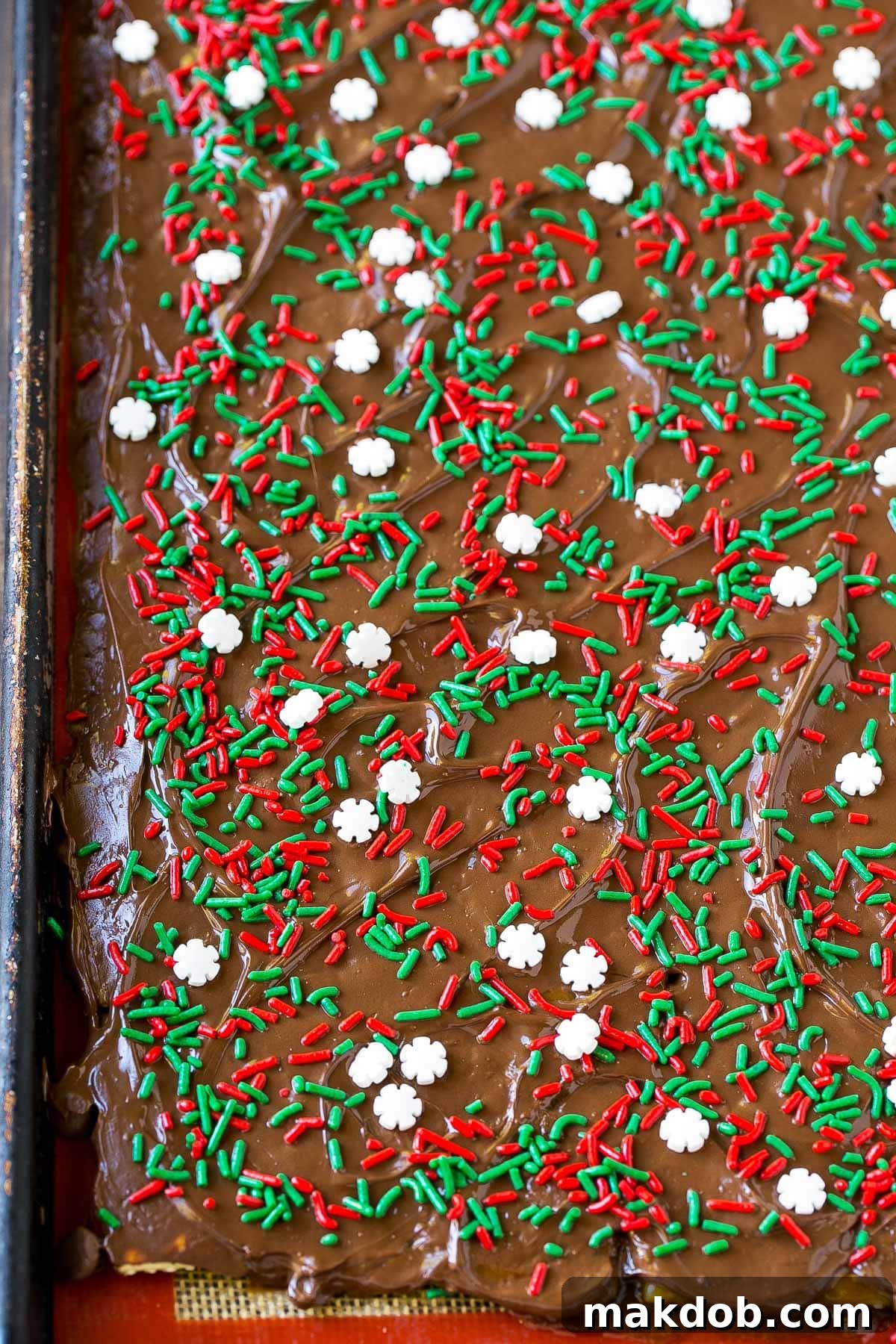 Irresistible Holiday Toffee Bark 5 A baking pan filled with golden toffee-covered crackers, generously topped with a layer of melted chocolate and vibrant holiday sprinkles.