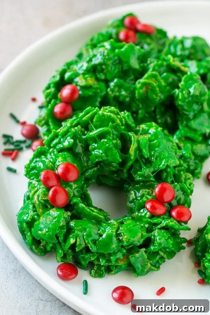 Christmas Wreath Cookies Recipe | Cornflake Wreaths | Cornflake Cookies | No Bake Cookie Recipe #cookies #wreath #christmas #holiday #nobake #dessert #dinneratthezoo Close-up of vibrant green Christmas wreath cookies with red candy berries on top, ready for a holiday celebration.