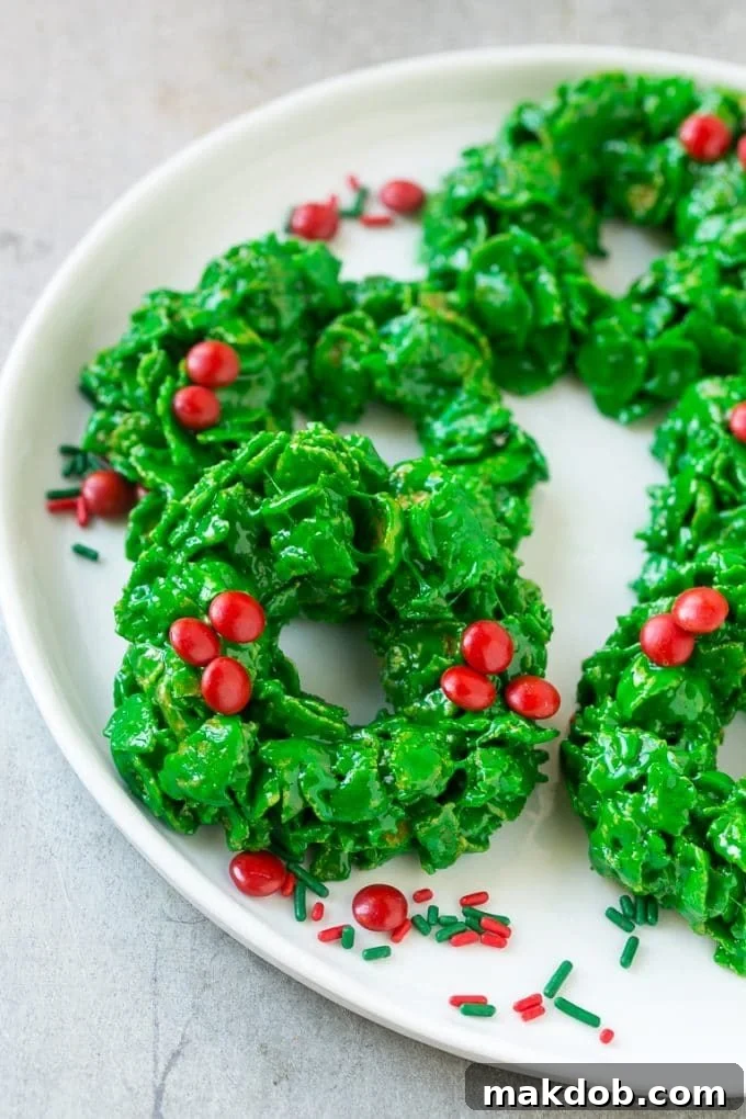 Christmas Wreath Cookies Recipe | Cornflake Wreaths | Cornflake Cookies | No Bake Cookie Recipe #cookies #wreath #christmas #holiday #nobake #dessert #dinneratthezoo A festive platter laden with beautifully shaped cornflake cookies resembling Christmas wreaths, adorned with red candies.