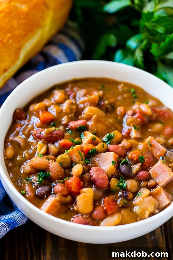 Slow Cooker Ham Bone Soup | Ham and Bean Soup | Ham Bone and Bean Soup | Ham Soup | Leftover Ham Recipe #ham #hamsoup #leftoverham #soup #slowcooker #crockpot #dinneratthezoo A close-up view of a rustic bowl of slow cooker ham bone soup, highlighting the generous portions of tender beans, vibrant vegetables, and savory ham in a rich broth, ready to provide ultimate comfort.
