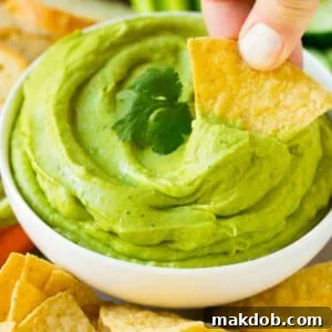 A tortilla chip scooping up a serving of avocado dip.