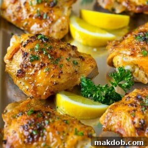 A pan of baked chicken thighs garnished with parsley and lemon.