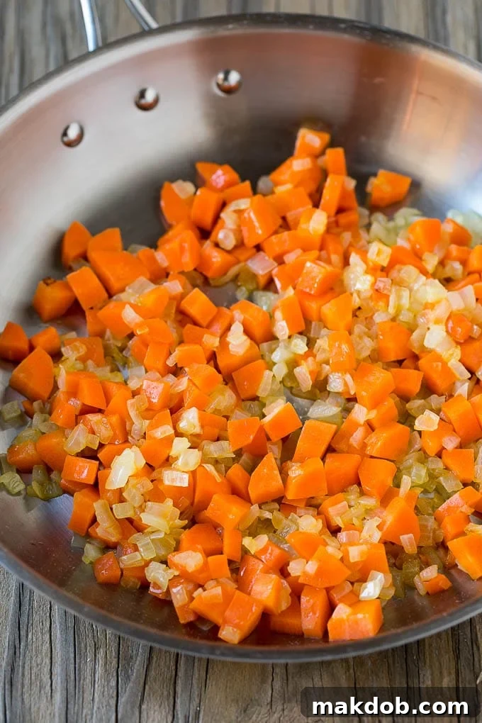 Guilt-Free Cauliflower Fried Rice 3 Finely chopped carrots, onion, and minced garlic simmering in a skillet, forming the flavor base for fried rice.