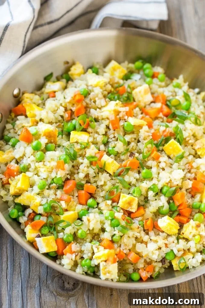 Guilt-Free Cauliflower Fried Rice 6 A large pan filled with vibrant cauliflower fried rice, featuring scrambled eggs, peas, carrots, and topped with fresh green onions.