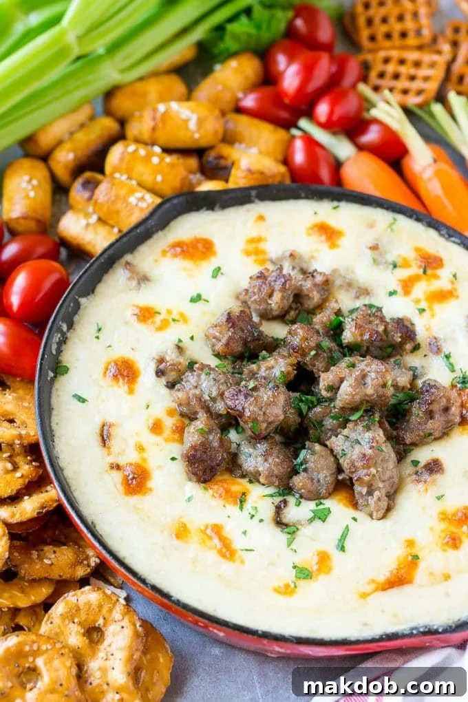 Rich and Creamy Beer Cheese Dip 4 A vibrant red skillet brimming with warm beer cheese dip, garnished with crumbled bratwurst and fresh parsley, served alongside an assortment of crisp vegetables and salty pretzels.