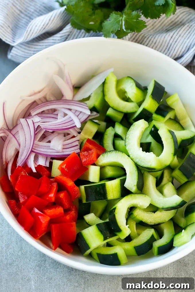 A vibrant bowl of sliced cucumbers, red peppers, and red onion, perfectly dressed and ready to serve.
