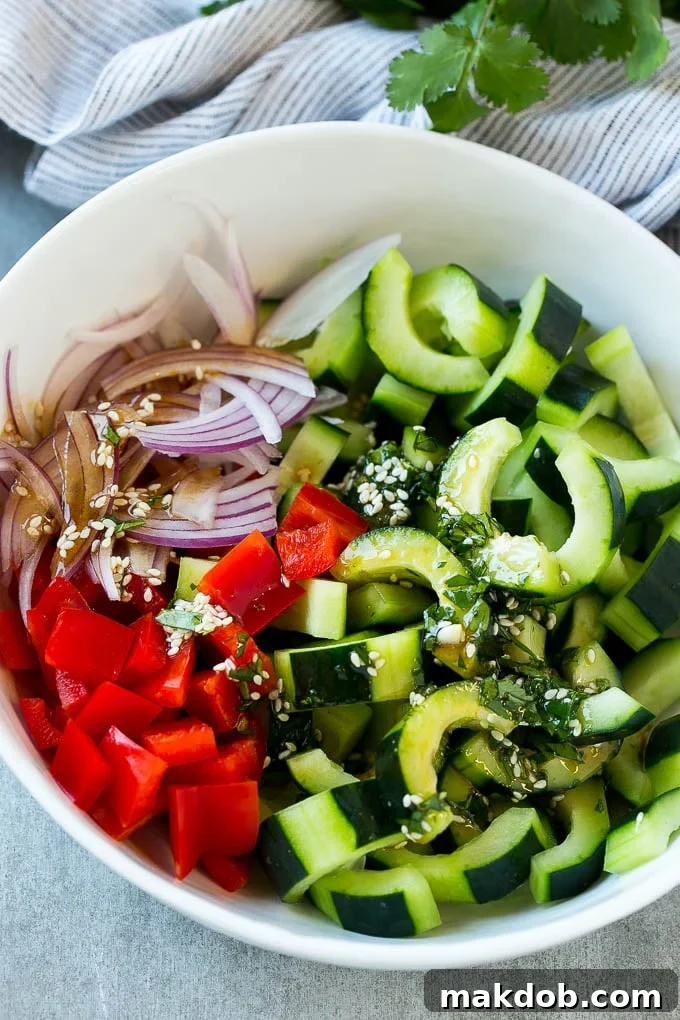 A bowl of freshly sliced cucumbers, vibrant red peppers, and thinly sliced red onions, glistening with a zesty dressing.