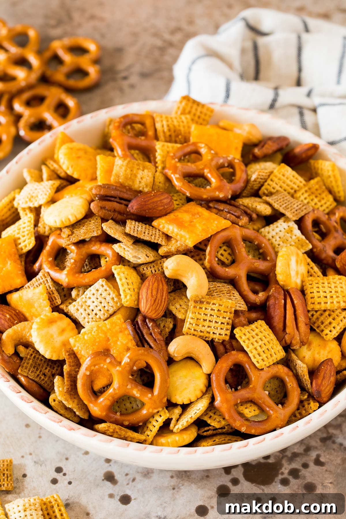 A large white bowl brimming with golden-brown homemade Chex mix, featuring a delightful assortment of cereals, crackers, pretzels, and nuts, perfectly seasoned and ready for snacking.