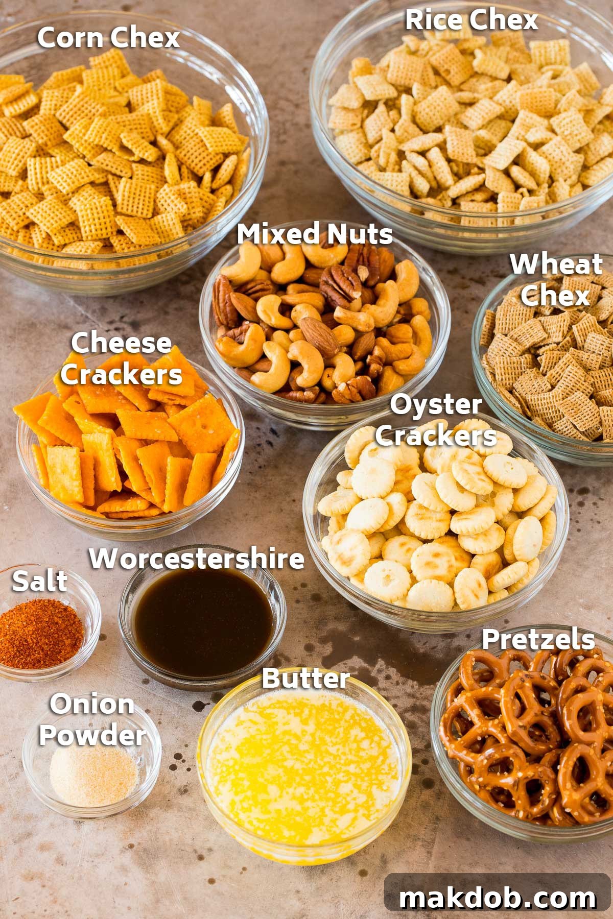Bowls of perfectly portioned ingredients for homemade Chex Mix, including different types of Chex cereal, oyster crackers, cheese crackers, pretzels, a mix of nuts, melted butter, Worcestershire sauce, seasoned salt, and onion powder, ready for mixing.