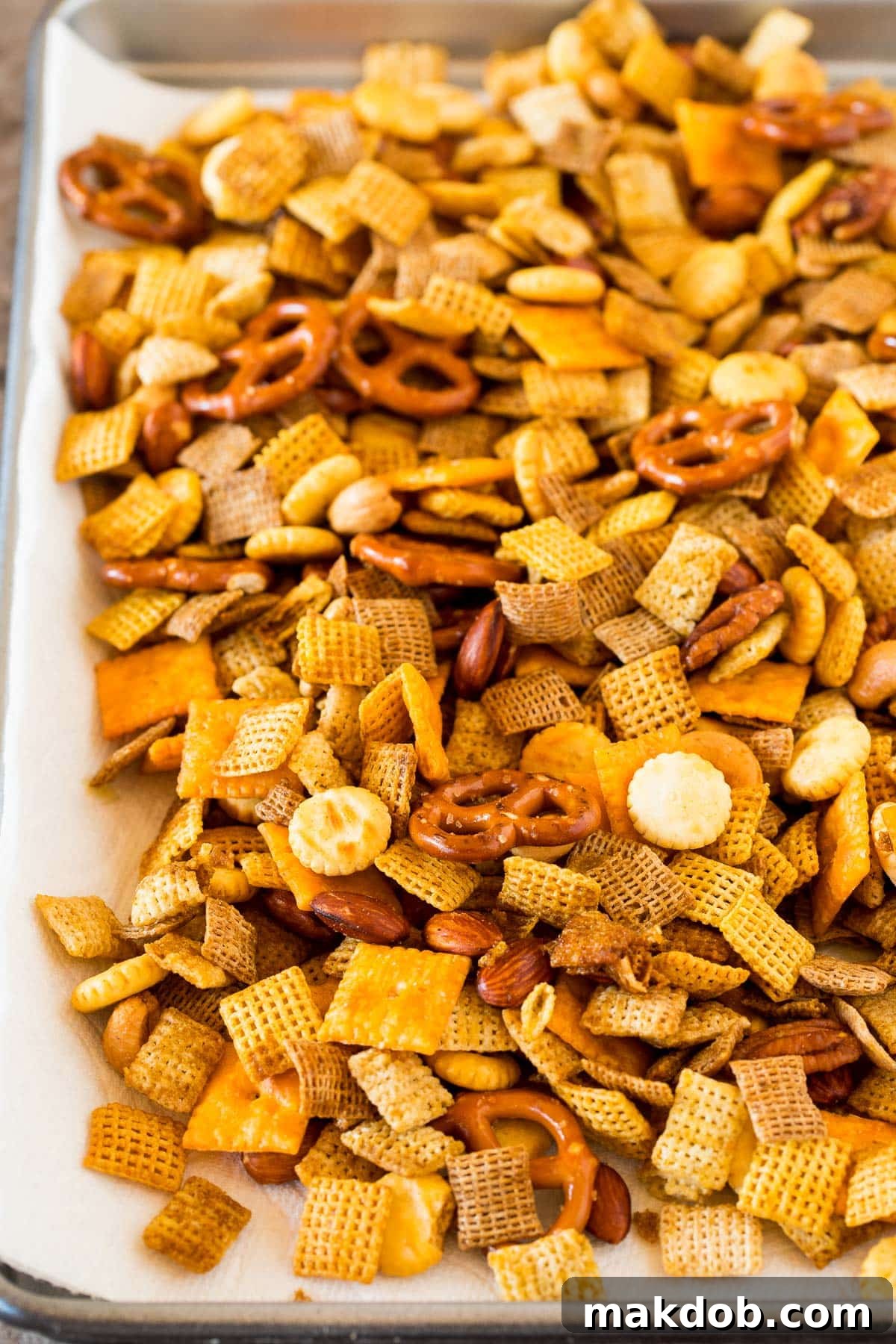 Freshly made Chex mix spread out on paper towels to cool, revealing its crunchy texture and rich seasoning. The mix is golden brown and aromatic.