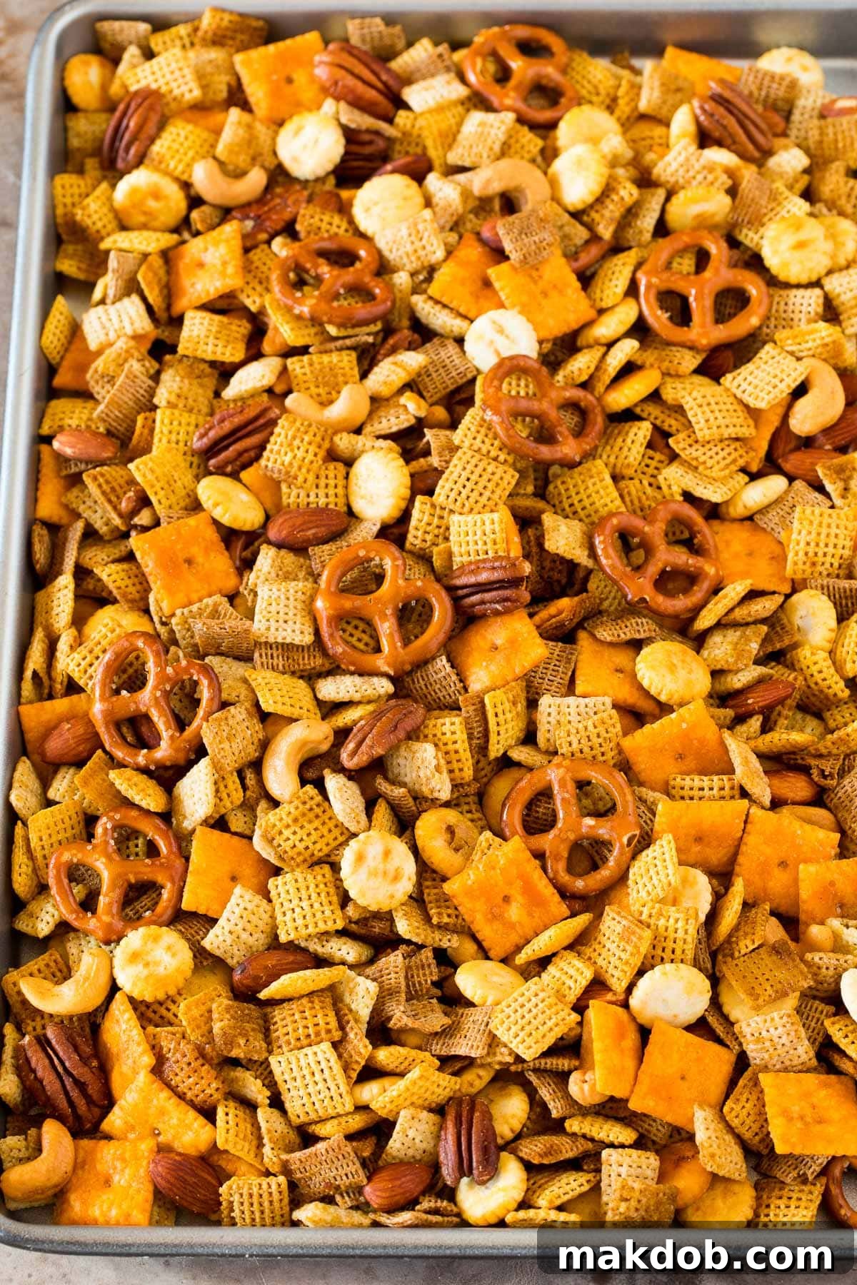 A large sheet pan filled with golden-brown homemade Chex mix, featuring a rich assortment of cereals, crackers, pretzels, and nuts.