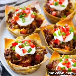 A plate of taco cups made with wontons, seasoned ground beef and cheese, topped with sour cream, tomatoes and green onions.